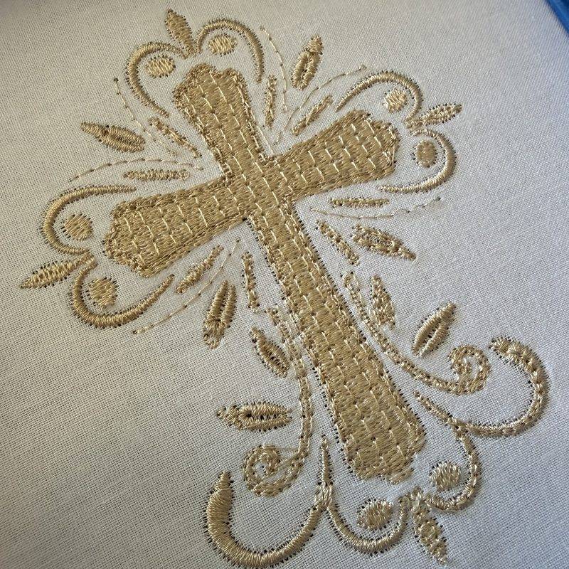 The same cross stitched in gold thread on white fabric, with a textured fill and satin scrolls